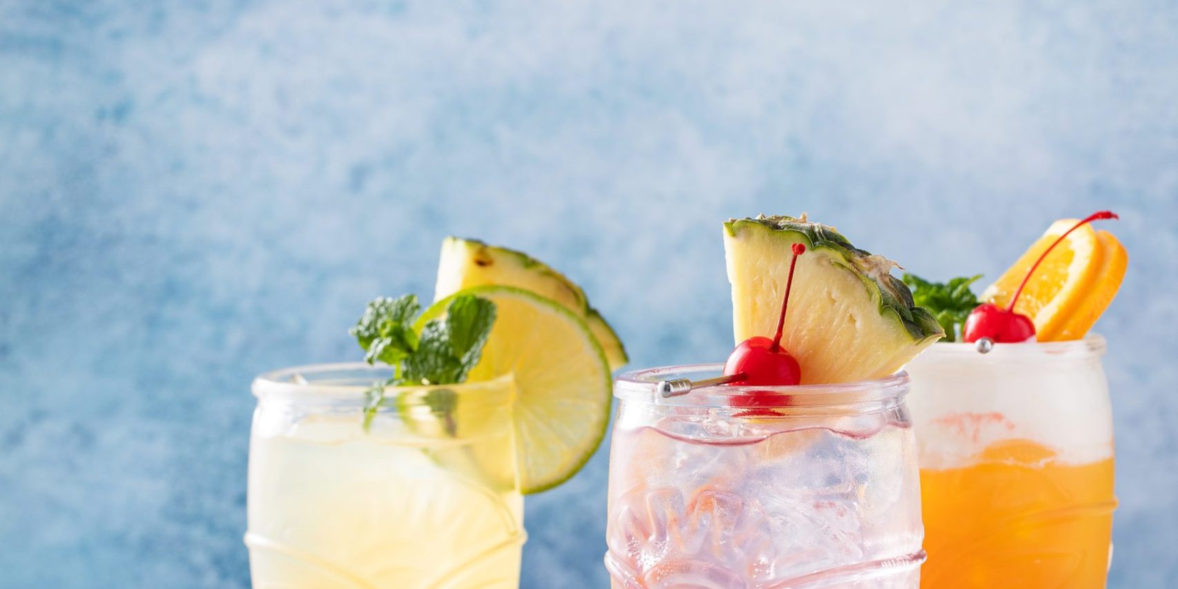 Variety of tropical tiki cocktails with cold foam, garnished with orange slices, cherry and mint